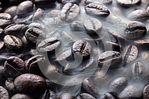 Fresh roasted coffee beans with smoke. Brown roasted coffee beans background. Coffee aroma.