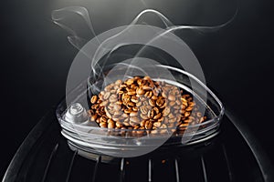 Fresh roasted coffee beans with smoke in coffeemaker bean container, close-up view photo