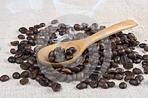 Fresh roasted coffee beans in wooden spoon smoke on retro desk