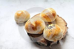 Fresh rolls, bread stacked on a piece of wood, light wheat bread, homemade flour pastries, buns sprinkled with white and black ses