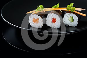 Fresh rolls on a plate, roll with salmon, cucumber and pepper served with carrot slices and parsley, black background