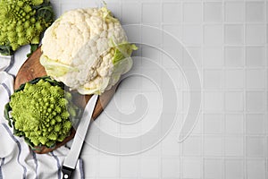 Fresh Romanesco broccoli and cauliflower on white tiled table, flat lay. Space for text