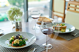 Fresh romantic breakfast table next to morning briliant light window, with beef, salmon fish, mashed potato, vegetable, red wine