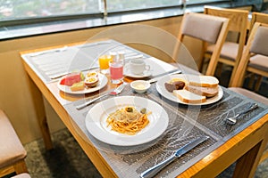 Fresh romantic breakfast table next to morning briliant light window, with bread, pastry, spaghetti, fruit, juice, coffee cup