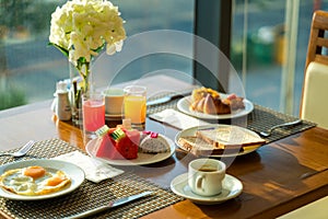 Fresh romantic breakfast table next to morning briliant light window, with coffee cup, bread, fruit, juice, egg