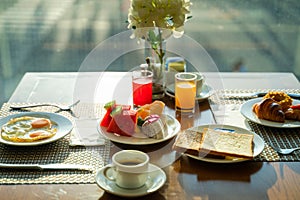 Fresh romantic breakfast table next to morning briliant light window, with coffee cup, bread, fruit, juice, egg