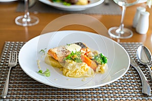 Fresh romantic breakfast table next to morning briliant light window, with salmon fish, mashed potato, vegetable, red wine