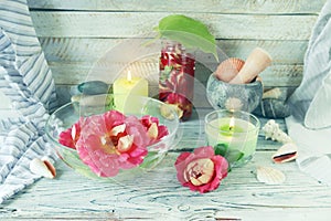 Fresh rose flowers and petal tincture, sea shells and stones, burning candles, on a wooden table, spa concept