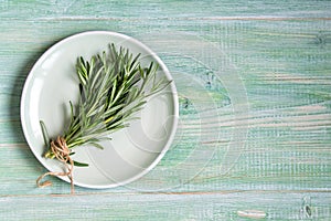 Fresh rosemary bunch on a plate on green wooden background, top view