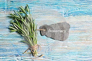 Fresh rosemary bunch with slate sign and text Rosemary on blue wooden background