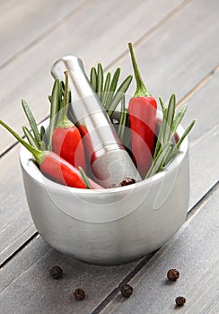 Fresh rosemary herb and red pepper in metal mortar with pestle