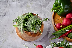 Fresh ruccola in a wooden bowl on white textured background, shallow depth of field.