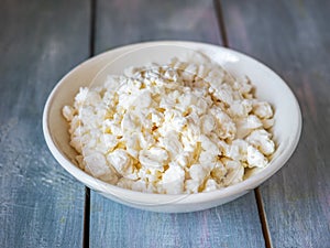 Fresh rustic cottage cheese in a white deep plate on a blue wooden table