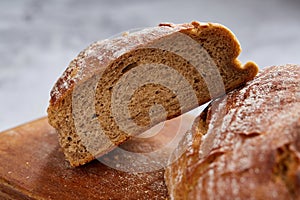 Fresh rye bread loaf on a wooden chopping board over white textured background, shallow depth of field