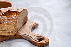 Fresh rye bread loaf on a wooden chopping board over white textured background, shallow depth of field