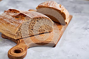 Fresh rye bread loaf on a wooden chopping board over white textured background, shallow depth of field