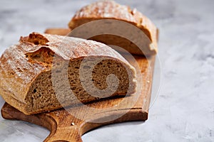 Fresh rye bread loaf on a wooden chopping board over white textured background, shallow depth of field