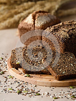 Fresh rye bread and three slices on a wooden board. There are a lot of scattered seeds around.