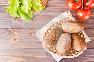 Fresh rye buns in a basket, salad and tomato on a wooden table