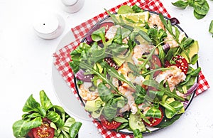 Fresh salad with avocado, shrimps, red tomatoes, arugula, lamb lettuce, red onion and sesame seeds on white table background. Top