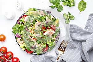 Fresh salad with avocado, shrimps, red tomatoes, arugula, lamb lettuce, red onion and sesame seeds on white table background. Top