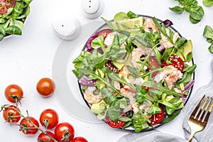 Fresh salad with avocado, shrimps, red tomatoes, arugula, lamb lettuce, red onion and sesame seeds on white table background. Top