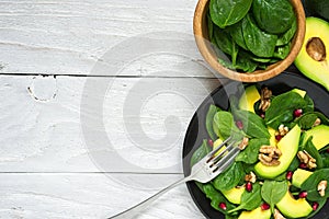 Fresh salad with avocado, spinach, pomegranate and walnuts in black plate with fork. healthy food