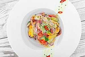 Fresh salad with avocado, sun dried tomatoes, hot peppers, cherry tomatoes, sweet peppers and onion on wooden background