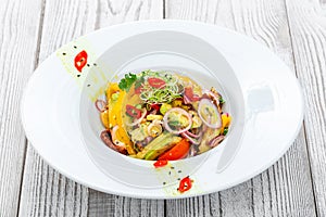 Fresh salad with avocado, sun dried tomatoes, hot peppers, cherry tomatoes, sweet peppers and onion on wooden background