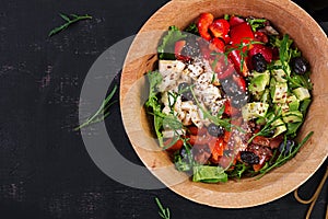 Fresh salad with avocado, tomatoes, mozzarella cheese, sweet peppers and black olives on wooden bowl. Top view, above