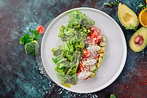 Fresh salad with cherry tomatoes, feta cheese, avocado on white plate on blue oxidized background