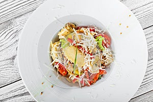 Fresh salad with chicken breast, artichokes, cherry tomatoes, lettuce and cheese parmesan on wooden background close up