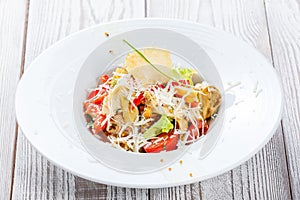 Fresh salad with chicken breast, artichokes, cherry tomatoes, lettuce and cheese parmesan on wooden background close up