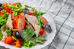 Fresh salad with chicken breast, arugula, black olives,red pepper, lettuce, fresh sald leaves and tomato on a white plate on woode