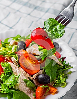 Fresh salad with chicken breast, arugula, black olives,red pepper, lettuce, fresh sald leaves and tomato on a white plate on woode