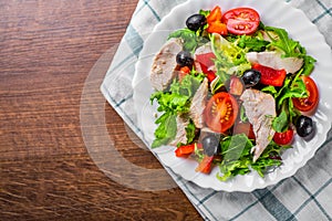 Fresh salad with chicken breast, arugula, black olives,red pepper, lettuce, fresh sald leaves and tomato on a white plate on woode