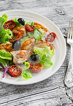 Fresh salad with chicken breast, sun-dried tomatoes, green salad and olives on a white plate