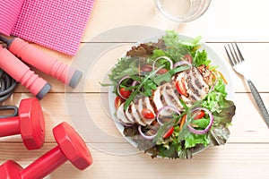 Fresh salad with chicken and fitness exercise equipments on wooden table