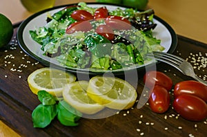 Fresh salad from different kinds of greens and a cherry tomato, dressed with olive oil and sprinkled with sesame seeds