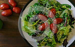 Fresh salad from different kinds of greens and a cherry tomato, dressed with olive oil and sprinkled with sesame seeds