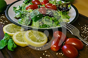 Fresh salad from different kinds of greens and a cherry tomato, dressed with olive oil and sprinkled with sesame seeds