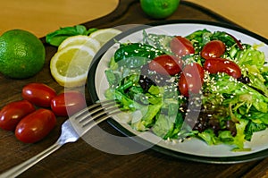 Fresh salad from different kinds of greens and a cherry tomato, dressed with olive oil and sprinkled with sesame seeds