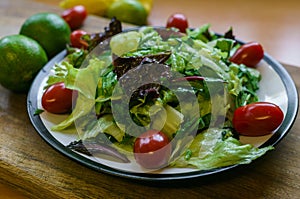 Fresh salad from different types of greens and cherry tomatoes, seasoned with olive oil and lime juice with lemon