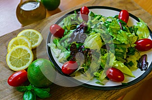 Fresh salad from different types of greens and cherry tomatoes, seasoned with olive oil and lime juice with lemon