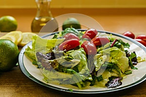 Fresh salad from different types of greens and cherry tomatoes, seasoned with olive oil and lime juice with lemon