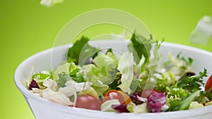 Fresh salad falling into bowl on green background