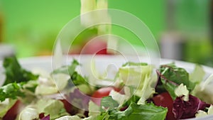 Fresh salad falling into bowl on green background