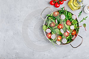 Fresh salad with green leaves of arugula, , spinach, beets, radish and tomato on a gray stone background