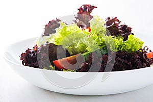 Fresh salad with green and purple lettuce, tomatoes and cucumbers on white wooden background close up.