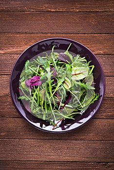 Fresh salad with mixed greens (arugula, mesclun, mache) on dark wooden background top view.